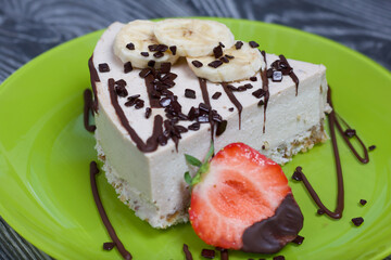 Cheesecake on a plate. Garnished with strawberries, bananas and chocolate. On brushed pine boards painted in black and white.