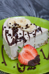 Cheesecake on a plate. Garnished with strawberries, bananas and chocolate. On brushed pine boards painted in black and white.