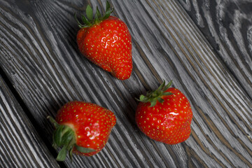 Red strawberry with green ponytails. On brushed pine boards painted in black and white.