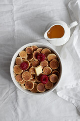 Bowl with tiny pancake cereal with raspberries on a white material. Trendy food. Mini cereal pancakes. Trendy breakfast