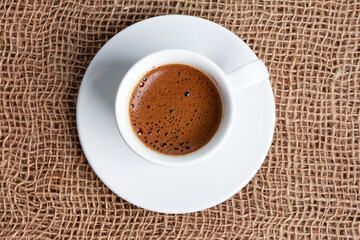 Espresso white cup on jute burlap sackcloth. Top view, single object. Coffee shop, morning, agriculture concept
