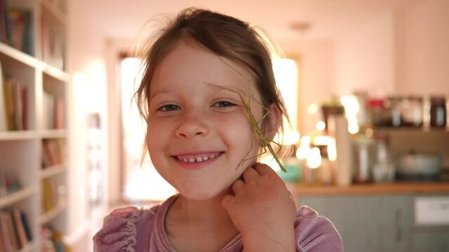 Cute kid girl portrait holds stick insect pet in hands and put it on her face at home have fun and smile