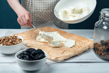 Woman spreads whipped sweet cream on meringue cake on a white vintage wooden table.