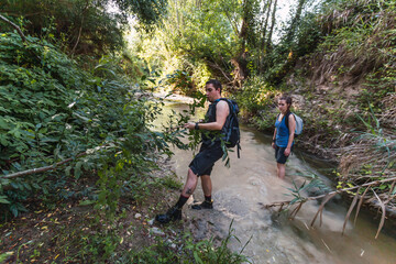 Naklejka na ściany i meble Small group of young tourists walking inside a river with little flow inside a forest in Spain in spring. Selective focus.