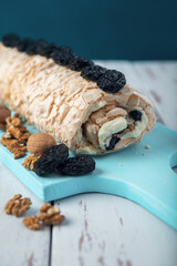 Prune-nut meringue roll on a blue cutting board on a white vintage wooden kitchen table.