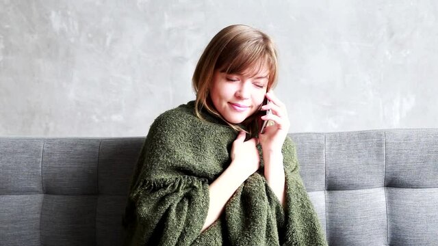 Happy bautiful young woman talking on cellphone while sitting on sofa in cozy room indoor. Close up portrait of Caucasian pretty girl speaking on phone during staying at home . Leisure concept