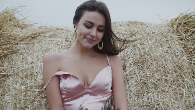 Portrait of elegant, smiling lady in dress with naked legs leaned on haystack