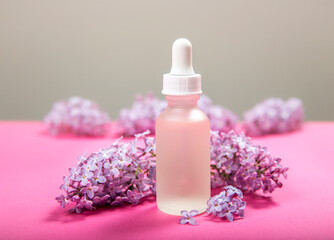 Obraz na płótnie Canvas Syringa known as lilac based beauty products concept. Small matte glass oil bottle with lilac blossom bundles for decoration on pink studio background.