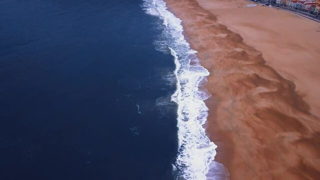 Flying over a sandy beach. Waves break on a sandy beach on the Atlantic coast, aerial View. Nazare, Portugal.