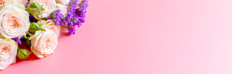 a bouquet of cream roses and bright purple flowers in full bloom on a pink background with space for text. greeting card. banner