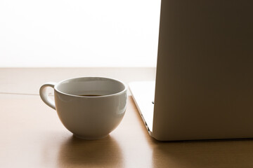 White office desk table with laptop computer, cup of black hot coffee 