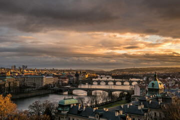 Golden sunset in Prague with dramatic sky from Letna park with Straka academy in the foreground. View of bridges over Vltava with Charles bridge. Czech Republic.