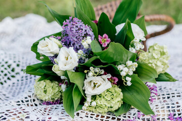 Delicate bouquet of lilac, Lily of the valley, eustoma, viburnum and saxifrage on a white lace shawl.Wicker basket in the background