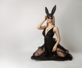 Beautiful blonde in a rabbit mask in a sexy evening dress on a white background