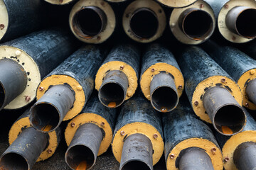 Heap of many new black insulated steel pipes at municipal construction site outdoors. Heating main...