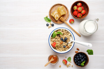 Granola with berries, milk and honeycombs. Bright healthy breakfast on white wooden background