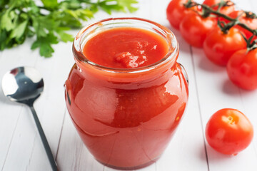 Tomatoes in their own juice or Tomato paste in a glass jar and fresh tomatoes on a white wooden table.