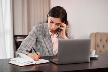 Fototapeta premium Businesswoman remote homework concept. Woman with a laptop.A young girl talking on the phone and writes in a notebook.