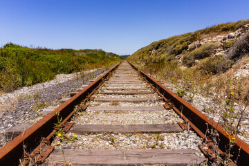An old red messy train track in the middle of the picture and two hills beside it on blue sky...