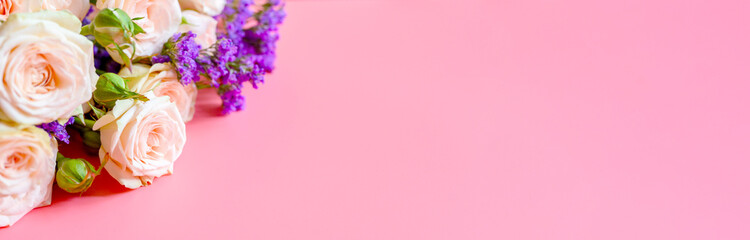 a bouquet of cream roses and bright purple flowers in full bloom on a pink background with space for text. greeting card. banner