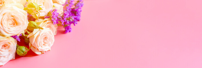 a bouquet of cream roses and bright purple flowers in full bloom on a pink background with space for text. greeting card. flare. banner