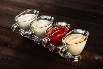 Four types of sauce in glass dishes on a dark wooden background