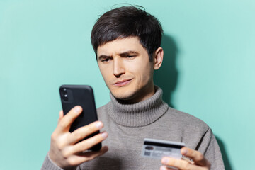 Studio portrait of young guy using smartphones and credit card on background of aqua menthe color.