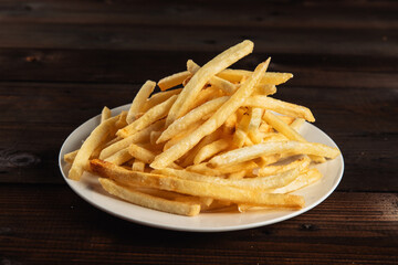 French fries on a white round plate on a dark wooden background