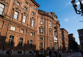 Fototapeta na wymiar Turin, Piedmont, Italy. May 2020. Palazzo Carignano, an imposing Baroque palace, it has a red brick facade characterized by wavy shapes. People wear the mask to protect themselves from the coronavirus