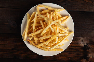 French fries on a white round plate on a dark wooden background