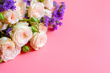a bouquet of cream roses and bright purple flowers in full bloom on a pink background with space for text. greeting card