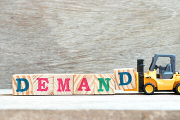 Toy forklift hold letter block d to complete word demand on wood background