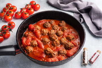 Delicious juicy Meatballs in tomato sauce are cooked in a cast iron pan. Close up Concrete background.