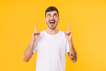 Photo of excited young man in eyeglasses pointing fingers upward