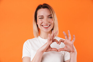 Image of pleased woman winking and making heart gesture with fingers