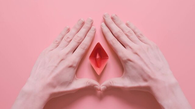 small red paper boat in female palms. conceptual abstract image of the vagina