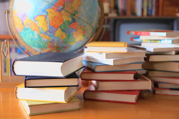 A close up of a pile of books on the table in the library Bookshelf and globe in the background selective focus and shallow depth of field