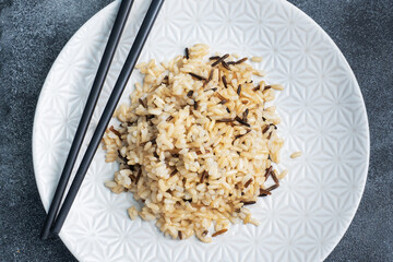 Brown and unpeeled rice on a plate with chopsticks. Dark concrete background. Copy space.