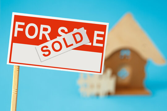 Real estate sale sign with sold sticker and house in the background
