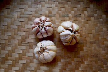Three whole bulb of white garlic (bawang putih) with closed cloves on a traditional handmade woven (anyaman) bamboo tray background top view. Rustic vintage, vegetable cooking ingredient.