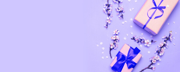 Flat lay gift box with blue ribbon on lilac background, cherry flower branch, top view with copy space. Father's Day gift.