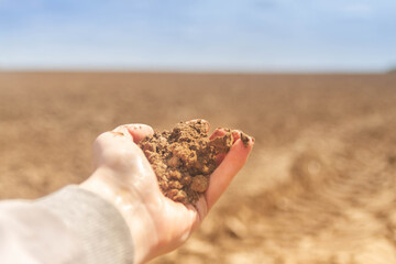 Plowed land close-up. Brown soil in the hand of a man. Poor infertile soil in the North of Russia.