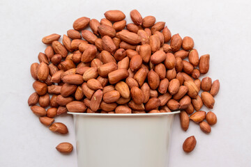 Peanut fruits in a plastic cup. Dark brown color, white background. Many edible seeds form a mountain. Concept of a healthy diet, vegetarianism, ingredient.