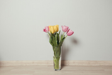 Beautiful yellow and pink tulips in glass vase on the floor in the room
