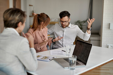 Young displeased couple arguing during a meeting with real estate agent.