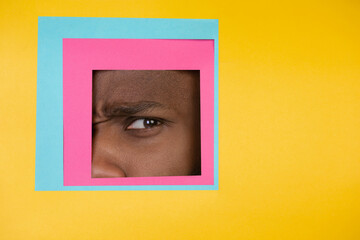 Scared. Eye of emotional african-american man peeks throught square in yellow background. Trendy geometrical style, copyspace. Vibrant colors. Sales, proposal, finance and business concept.