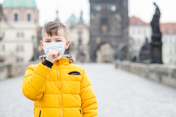 Coughing boy wearing medical protective mask on Charles Bridge in Prague. Coronavirus epidemic...