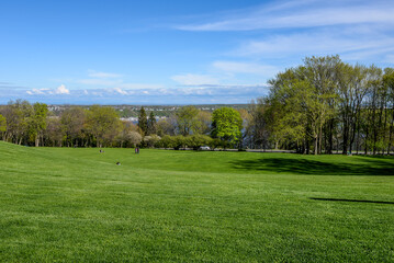Fototapeta na wymiar Rolling grassy hill and trees in Battlefields Park with blue sky, clouds and a view overlooking Quebec, Canada.