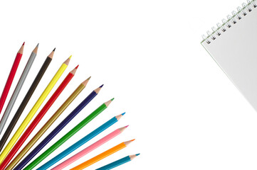 Wooden color pencils on a white isolated background lie like a fan and a notebook.