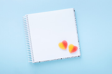Notebook with colorful gummy hearts on blue background. Mock up. Top view. Copy space